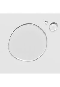 Transparente Wassertröpfchen auf einer glatten, weißen Oberfläche. Ein großer, unregelmäßiger Tropfen wird von zwei kleineren, runden Tropfen begleitet.