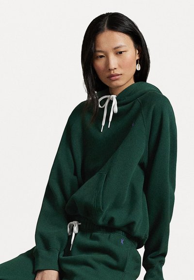 Green hoodie with a drawstring and front pocket, made of soft material. Paired with matching sweatpants, featuring a small logo detail.
