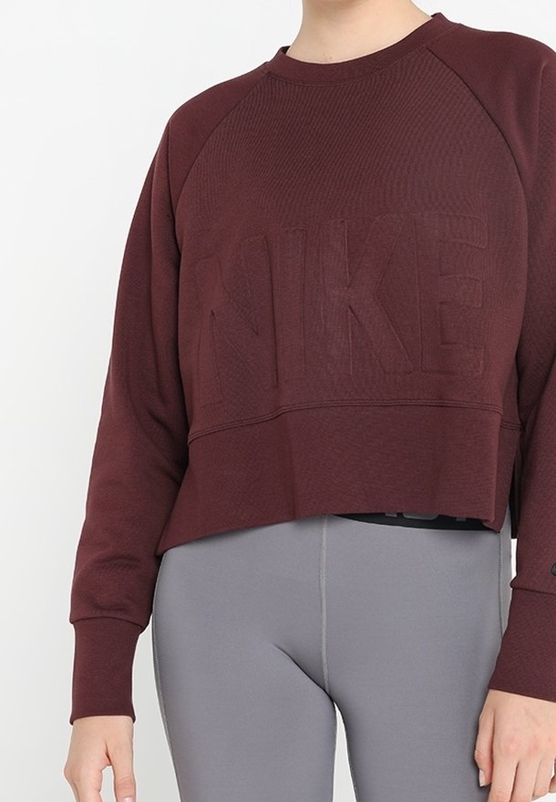 Sudadera corta de color burdeos hecha de tela texturizada con un logotipo "NIKE" en relieve. Combinada con leggings de talle alto en gris.