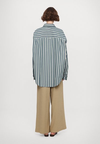 Striped skjorte med knapper i blått, grønt og hvitt. Løs passform, lange ermer og buet kant. Brukt med vide beige bukser.