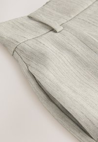 Gray herringbone fabric with a smooth texture features a folded waistband and a flat front, showcasing tailored pleats.