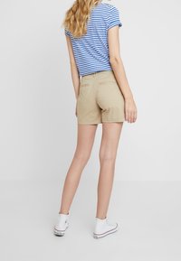 Beige shorts med lige snit og baglommer. Kombineret med en blå- og hvidstribet t-shirt og hvide sneakers.
