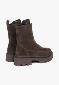 Brązowe zamszowe botki za kostkę z grubą, teksturowaną podeszwą, wkładkami do ściągania i eleganckim designem. Charakterystyczne dla czystych linii i nowoczesnej sylwetki.