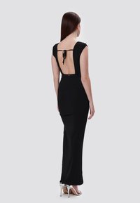 Schwarzes, tailliertes Kleid mit einem Rückenausschnitt, Kapellosenärmeln und einem Satinband. Glattes Material, knöchellang, kombiniert mit silbernen High-Heels.
