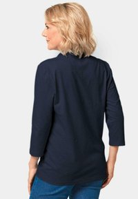 Marineblaues, langärmeliges Oberteil mit rundem Ausschnitt, das eine glatte Textur und eine lockere Passform aufweist, kombiniert mit blauen Jeans.