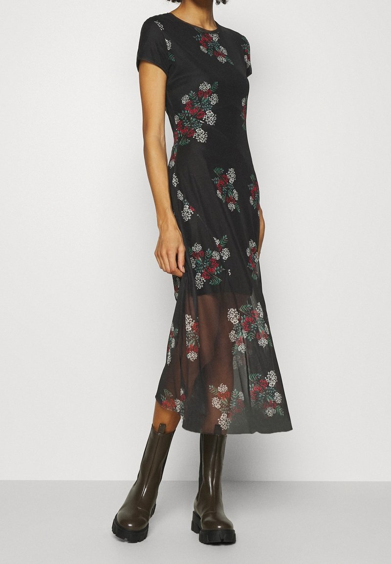 Svart blommig klänning med korta ärmar, prydd med röda och vita blommor samt gröna blad. Flikig, genomskinlig nederdel, kombinerad med bruna knähöga stövlar.