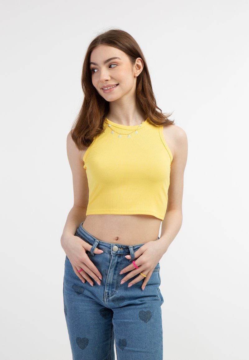Žlutý žebrovaný crop top s kulatým výstřihem a dekorativními květinovými ozdobami, spárovaný s džíny s vysokým pasem a srdíčkovým vzorem.