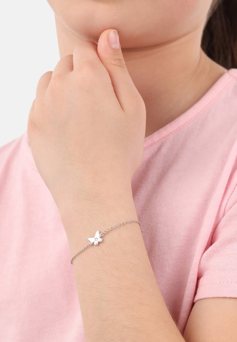 Braccialetto in argento con un charm a forma di farfalla e un piccolo accento di pietra preziosa, indossato su una mano contro una camicia rosa.