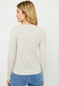 Top a maniche lunghe con strisce orizzontali beige e bianche, scollo rotondo, tessuto morbido e design aderente. Indossato con jeans blu.