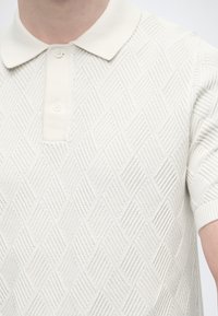 Λευκό polo με κοντά μανίκια, υφασμένο με μοτίβο διαμαντιών και ριμπ γιακά, με δύο κουμπιά στο λαιμό.