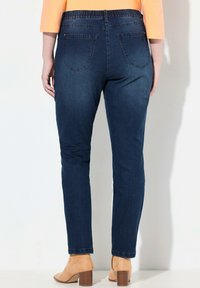 Ciemnoniebieskie dżinsy z miękkim elastycznym pasem, wąski krój i dwie tylne kieszenie, zestawione z brązowymi botkami na obcasie.