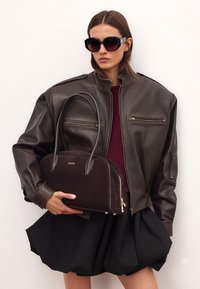 Smeđi kožni avijatičarski kaput, bordo pulover, crna razgibana suknja i tamnosmeđa nubuk torba s kožnim ručkama i zlatnim detaljima.