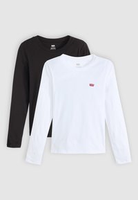 Twee T-shirts met lange mouwen: één zwart en één wit, beide gemaakt van katoen met ronde halslijnen. Elke heeft een klein rood logo op de borst.