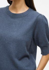 Pull en tricot bleu marine avec un col rond et des manches courtes bouffantes, présentant une texture douce et une finition côtelée autour du col.