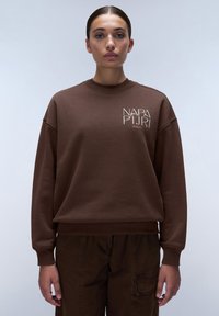 Brun sweatshirt med rund hals, med en vit logotyp på bröstet. Tillverkad av mjukt material har den sänka axlar och ribbade ärmslut.