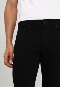 Svarta jeans i denim med smal passform, femfickorsdesign och kontrasterande sömnad. Främre knappstängning och bältesöglor är synliga.