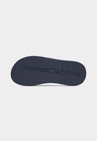 Σκούρα λαστιχένια σόλα παπουτσιού με υφή από οριζόντιες γραμμές και χαραγμένο κείμενο "TOMMY HILFIGER" στο κάτω μέρος.