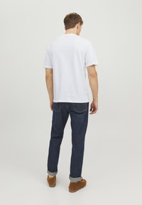 Hvid bomulds T-shirt med korte ærmer, set fra ryggen. Båret med mørkeblå denim jeans og brune ruskinds sko med optrillede manchetter.