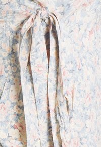 Blommig omslagsklänning i ljusblått med rosa och vita blommor. Knyt i midjan med långa, texturerade band för justerbar passform. Mjukt och lätt tyg.