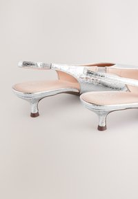 Sølvmetalliske slingback-hæle med tekstureret finish, lav stiletthæl og en glat, lysefarvet indersål.