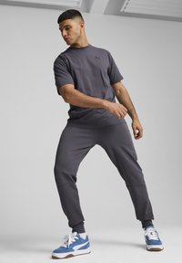 Grijze sportshirt met korte mouwen en bijpassende joggingsbroek, met een strakke pasvorm. Blauwe en witte sneakers met bruine zolen.