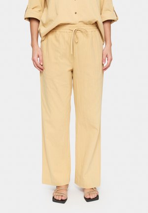 Pantaloni ampi di colore giallo chiaro con vita elastica e coulisse. Realizzati in morbido tessuto, con una consistenza liscia e una vestibilità rilassata.
