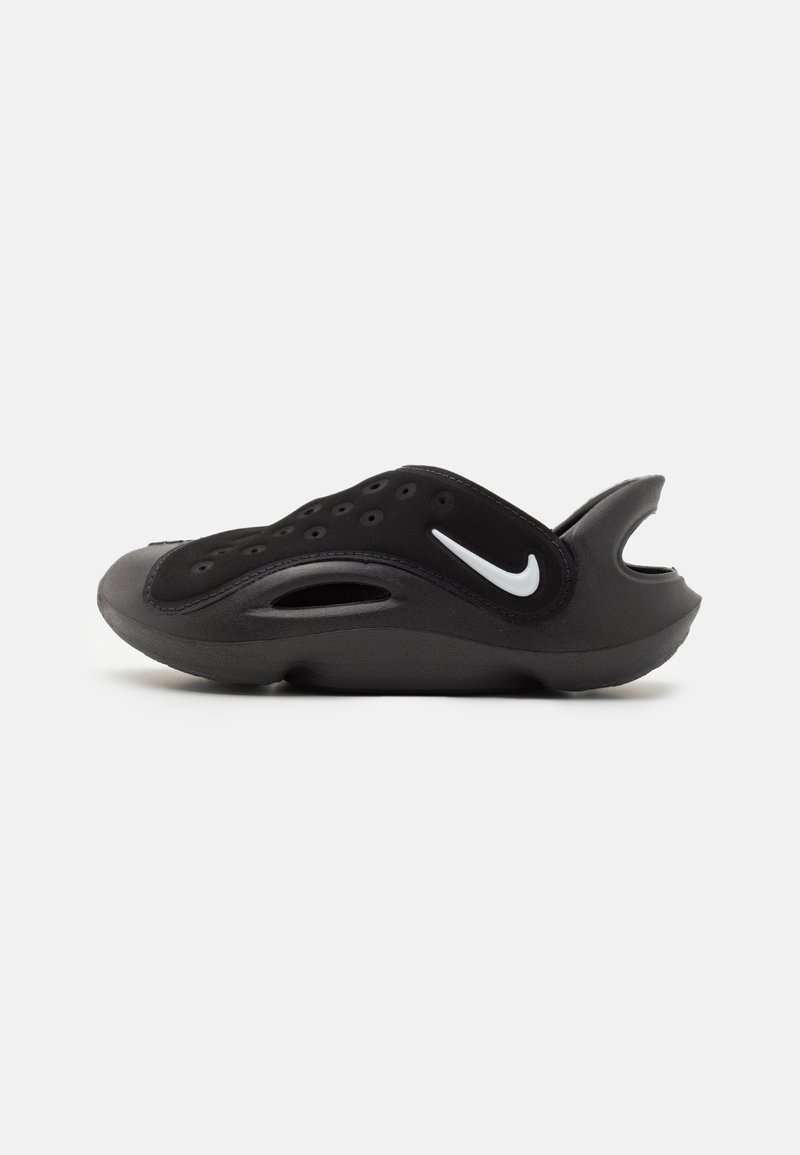 Black slip-on shoe with a sleek design, featuring a textured upper, ventilation holes, and a prominent white Nike swoosh on the side.