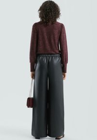 Bordowy sweter o fakturze z bufkami na rękawach, zestawiony z czarnymi szerokimi spodniami ze sztucznej skóry oraz małą bordową torebką na łańcuszku.