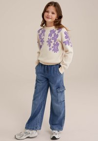 Pulover: kremast z vijoličnimi cvetličnimi vezeninami; sproščen kroj. Hlače: modri viskozni denim, širokega kroja s žepi. Teniske: siva in bela.