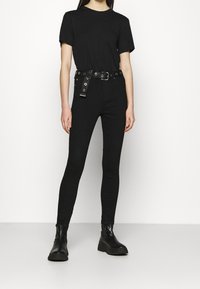 Camiseta negra combinada con jeans pitillo negros con cinturón de hebilla. La modelo lleva botines negros gruesos. Atuendo sencillo y monocromático.