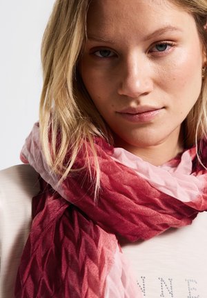 Bufanda en degradado de rojo y rosa con un patrón texturizado en forma de diamante. El tejido ligero cae suavemente alrededor del cuello, complementado por una blusa ligera.