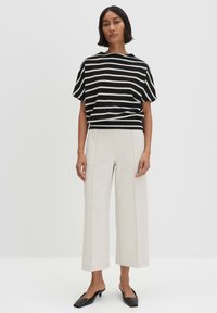 Zwart-witte gestreepte T-shirt met korte mouwen in een losse pasvorm, gecombineerd met roomkleurige wijde broekspijpen en platte zwarte schoenen. Soepele, lichte stof.