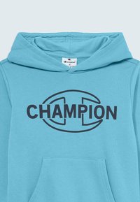 Svetlo modra majica s kapuco in velikim črnim logotipom "CHAMPION" na sprednji strani. Ima sprednji žep in mehak teksturiran material.