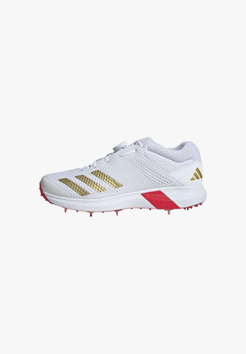 White athletic shoes feature gold stripes, a textured mesh upper, red accents on the sole, and metal spikes for traction.