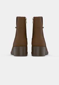 Καφέ μποτάκια μέχρι τον αστράγαλο με λεία, ματ υφή, στρογγυλή μύτη και τετράγωνη φτέρνα. Διαθέτουν δύο πίσω φερμουάρ και διακριτικές ραφές.