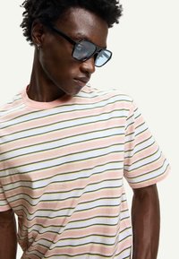 Striped t-shirt featuring pink, white, and green horizontal lines, made of soft fabric with short sleeves and a crew neckline. Black sunglasses worn.