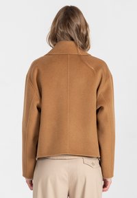 Krótka kurtka z brązowej mieszanki wełny z szerokim kołnierzem, opuszczonymi ramionami i gładką fakturą. Posiada prosty dół i minimalne detale przeszyć.