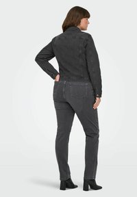 Crna traper jakna sa strukturiranim dizajnom, u kombinaciji sa slim-fit crnim hlačama. Model stoji sa rukama u džepovima, prikazujući pogled sa leđa.