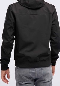 Svart huva-jacka med en slät textur, som har ribbad nederkant och manschetter, samt en broderad logga på vänster ärm.