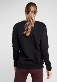 Sudadera negra de manga larga, con puños y dobladillo de canalé. Textura suave, ajuste relajado, vista posterior, combinada con leggings burdeos.