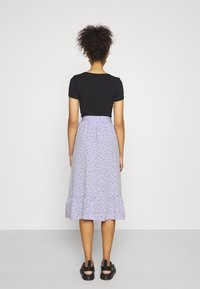 Musta tiukka toppi yhdistettynä lilaan hameeseen, jossa on kukkakuosi ja röyhelöhelma, sekä mustat sandaalit.