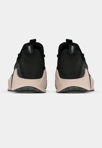 Ζεύγος μαύρων και μπεζ αθλητικών παπουτσιών Nike, εμφανιζόμενο από το πίσω μέρος με θηλιές και σπογγώδη σόλα σε λευκό φόντο.