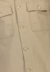 Beige button-up shirt featuring a textured fabric, two chest pockets, and five matching buttons along the front placket.