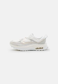 Hvide og lysegrå sneakers med mesh- og ruskindsteksturer, der har en synlig luftenhed, buet design og subtile guld accenter.