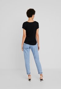 Černý top s krátkým rukávem, měkký materiál, volný střih, v kombinaci se světle modrými tapered džíny a černými sandály na podpatku s bílými akcenty.