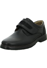 Scarpa in pelle nera con punta arrotondata, cinturino in velcro e superiore texture. Presenta una soletta imbottita e una resistente suola in gomma.