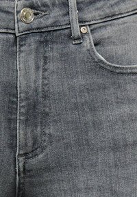 Tumši pelēkas džinsa bikses ar gludu tekstūru, priekšpusē ar kabatu, metāla pogas aizdari un smalkām šuvju detaļām.