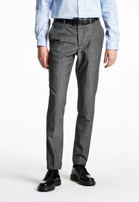 Pantaloni grigi su misura con un sottile motivo a quadri, vestibilità slim e tessuto liscio; abbinati a scarpe nere stringate e una camicia azzurro chiaro.