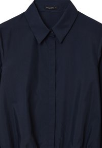 Camicia colletto blu navy realizzata in tessuto morbido, con chiusura a bottoni sul davanti e un dettaglio in vita leggermente arricciato. Etichetta della taglia visibile.