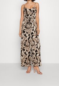 Vestido maxi floral en negro y beige con escote volado, tirantes de spaghetti ajustables y cinturilla anudada. Combinado con sandalias de color claro.